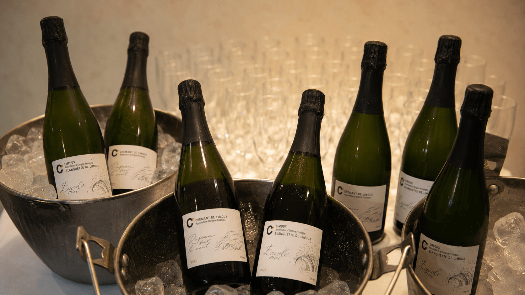 Бутылки Crémant de Limoux и Blanquette de Limoux Cazaban охлаждаются в металлических вёдрах со льдом на фоне бокалов.
